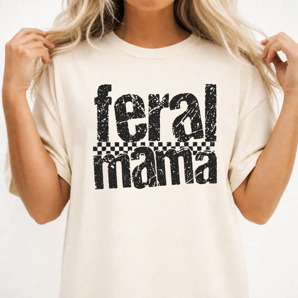 Woman wearing an ivory shirt with bold distressed Feral Mama lettering and a checkered stripe accent on the front