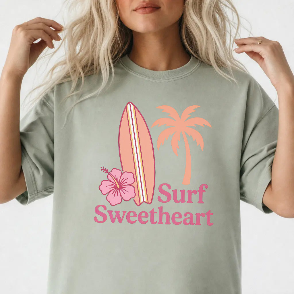 Woman wearing a bay blue Surf Sweetheart graphic tee with retro surfboard and hibiscus design