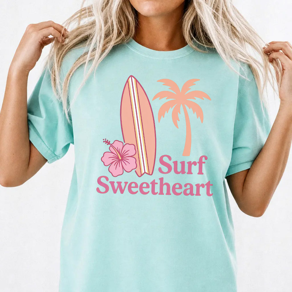 Woman wearing a chalky mint Surf Sweetheart graphic tee with retro surfboard and hibiscus design