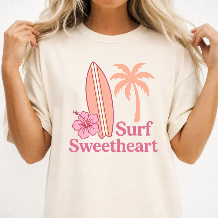 Woman wearing an ivory Surf Sweetheart graphic tee with retro surfboard and hibiscus design