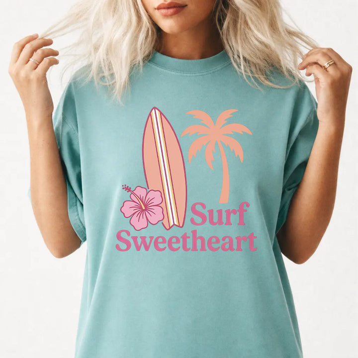 Woman wearing a seafoam Surf Sweetheart graphic tee with retro surfboard and hibiscus design