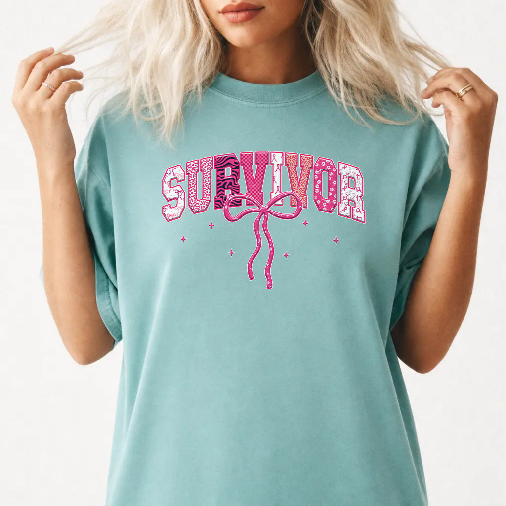 Woman wearing a seafoam survivor pink ribbon graphic tee with varsity lettering and pink bow