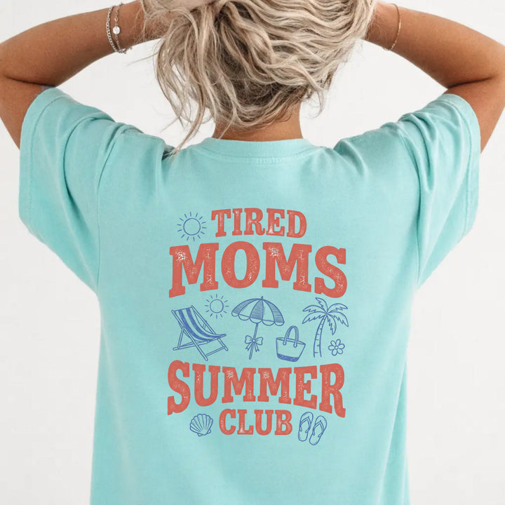 Woman wearing a chalky mint Tired Moms Summer Club graphic tee with beach doodle back print
