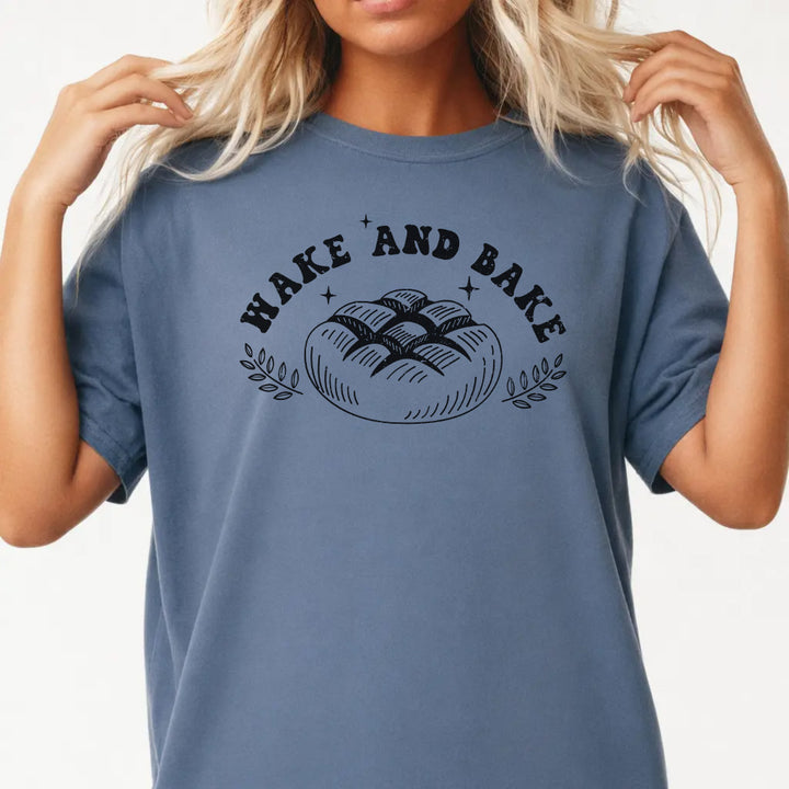 Woman wearing a blue jean shirt with a rustic artisan bread loaf illustration and the phrase Wake and Bake on the front