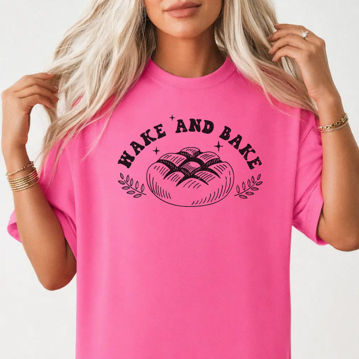 Woman wearing a neon pink shirt with a rustic artisan bread loaf illustration and the phrase Wake and Bake on the front