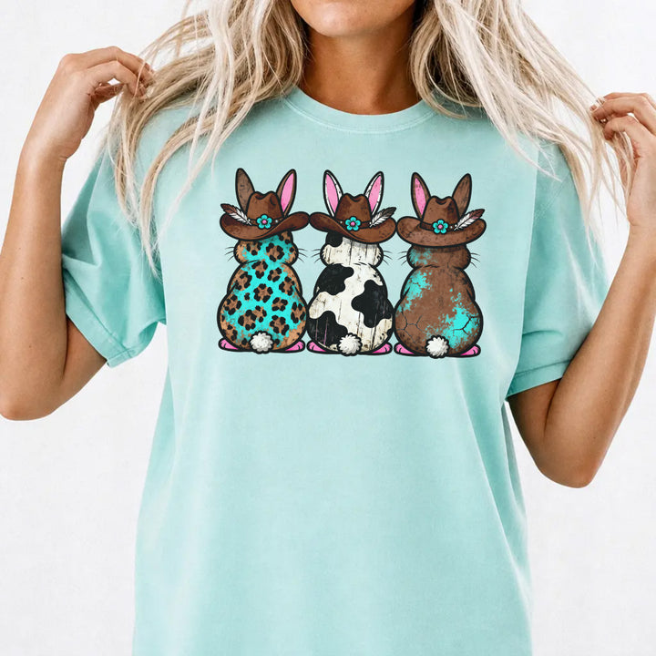 Woman wearing a chalky mint shirt with three western Easter bunnies in cowboy hats featuring leopard cowhide and turquoise patterns on the front
