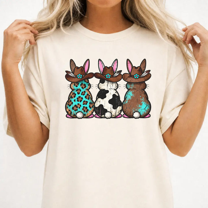 Woman wearing an ivory shirt with three western Easter bunnies in cowboy hats featuring leopard cowhide and turquoise patterns on the front