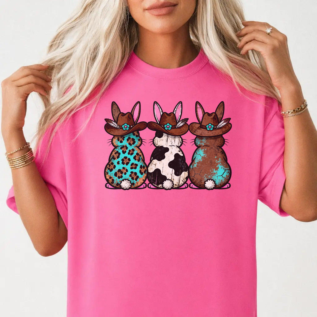 Woman wearing a neon pink shirt with three western Easter bunnies in cowboy hats featuring leopard cowhide and turquoise patterns on the front