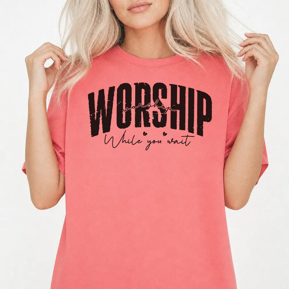 Woman wearing a watermelon shirt with bold distressed lettering and script text that reads Worship While You Wait on the front