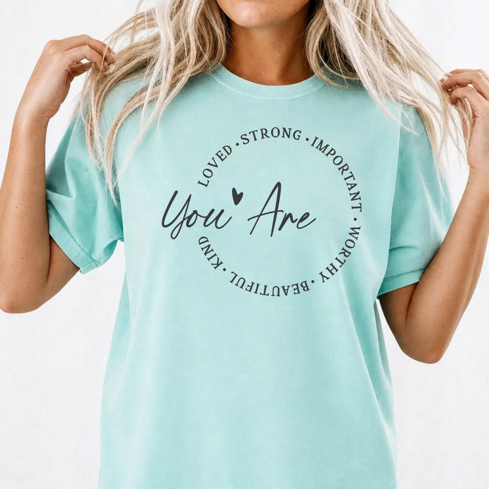 Woman wearing a chalky mint shirt with a circle of affirmation words including loved strong worthy and beautiful around the script phrase You Are on the front