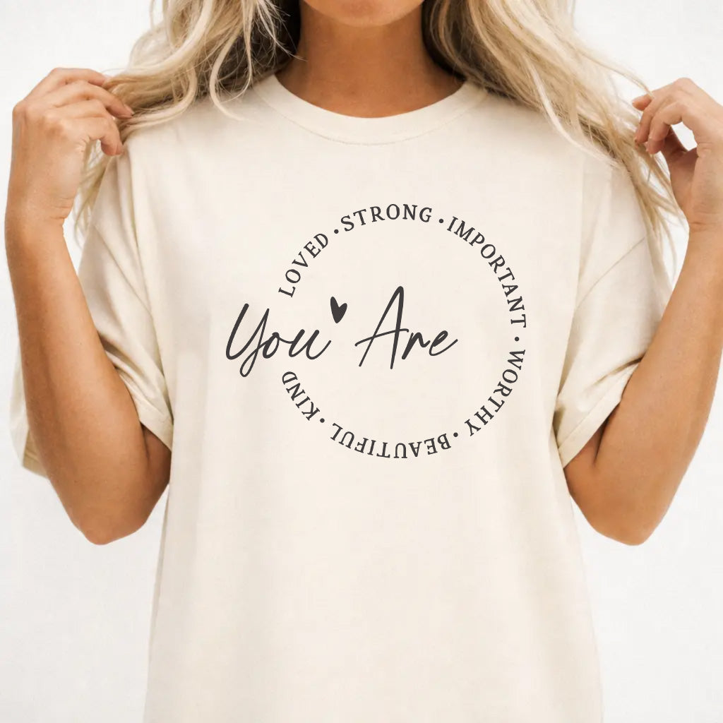 Woman wearing an ivory shirt with a circle of affirmation words including loved strong worthy and beautiful around the script phrase You Are on the front