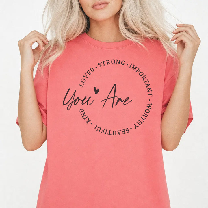 Woman wearing a watermelon shirt with a circle of affirmation words including loved strong worthy and beautiful around the script phrase You Are on the front