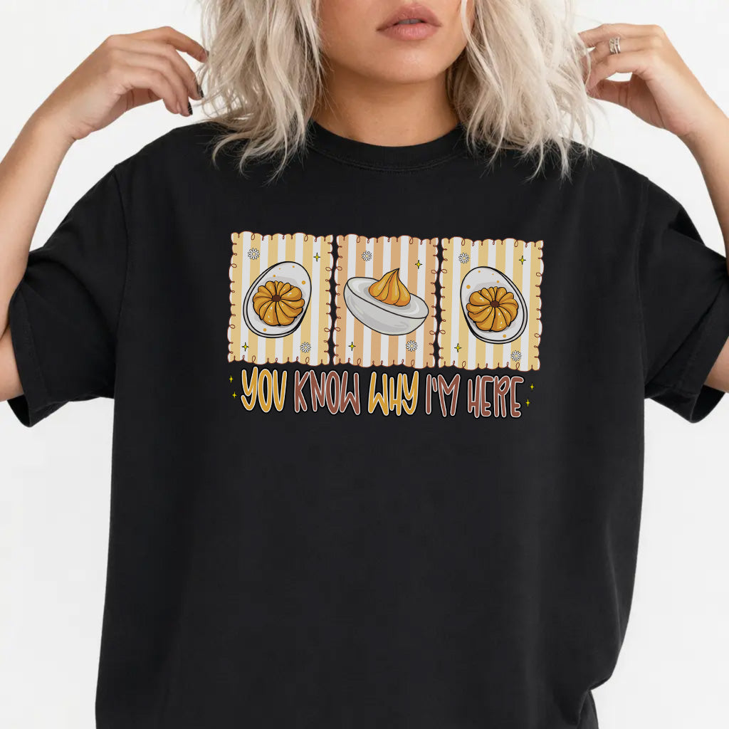 Woman wearing a black graphic tee with a retro deviled egg illustration and the phrase You Know Why Im Here on the front
