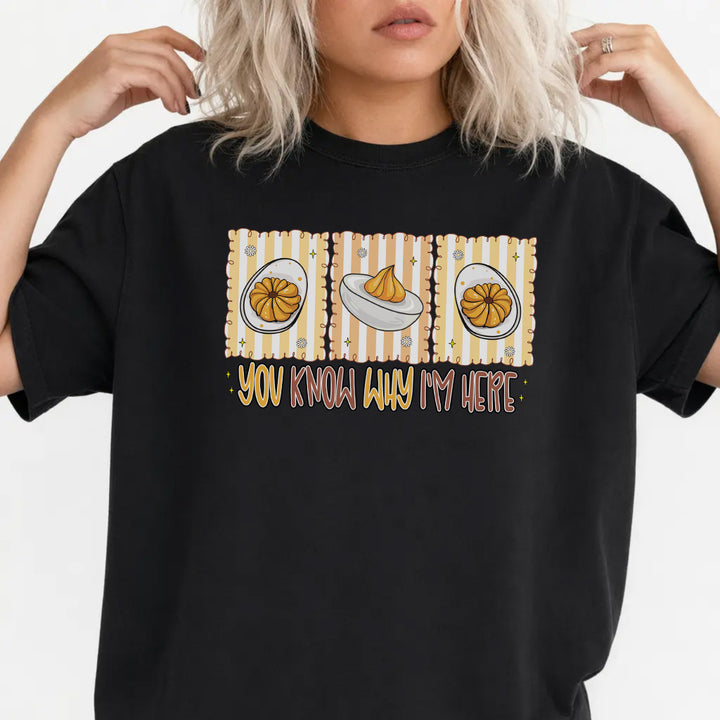 Woman wearing a black graphic tee with a retro deviled egg illustration and the phrase You Know Why Im Here on the front