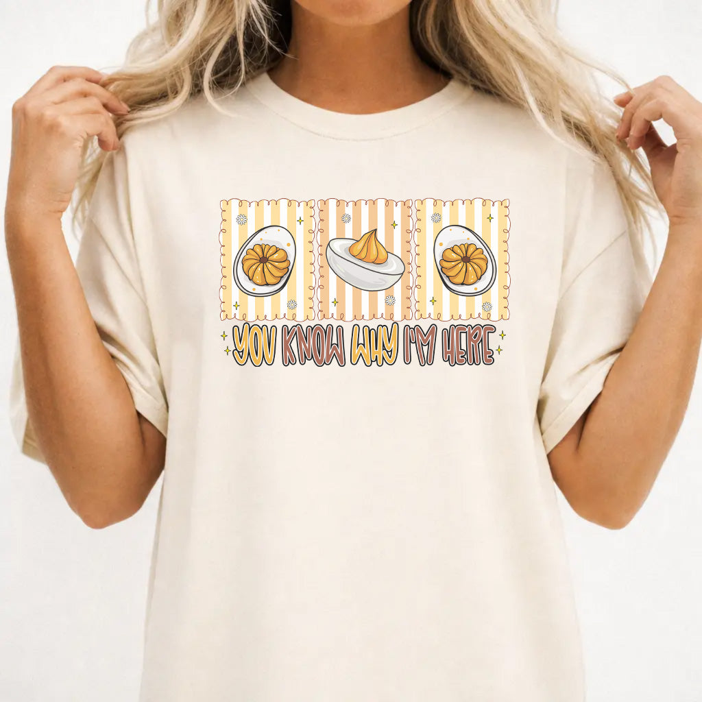 Woman wearing an ivory graphic tee with a retro deviled egg illustration and the phrase You Know Why Im Here on the front