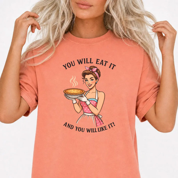 Woman wearing a terracotta graphic tee with a retro pin-up woman holding a pie and the phrase You Will Eat It and You Will Like It on the front