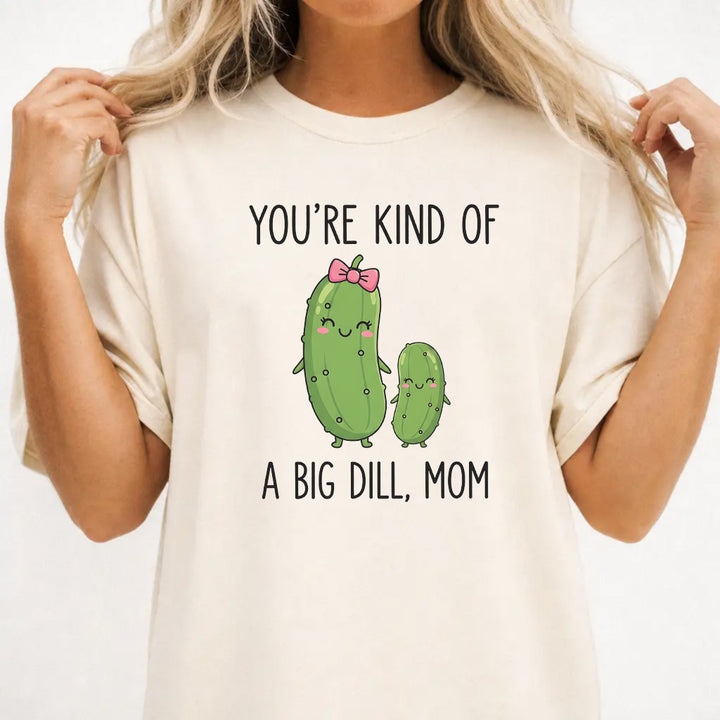 Woman wearing an ivory graphic tee with cute pickle characters and the phrase Youre Kind of a Big Dill Mom on the front