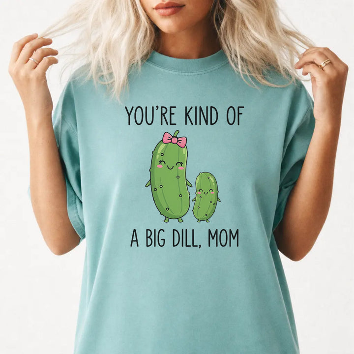 Woman wearing a seafoam graphic tee with cute pickle characters and the phrase Youre Kind of a Big Dill Mom on the front